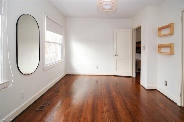 empty room featuring wood-type flooring, visible vents, and baseboards