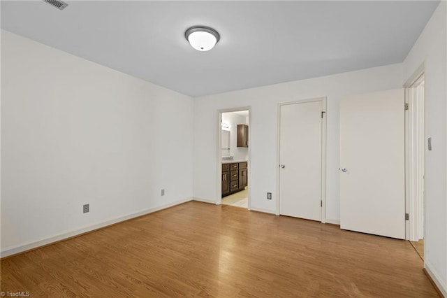 unfurnished bedroom featuring ensuite bathroom and light hardwood / wood-style floors