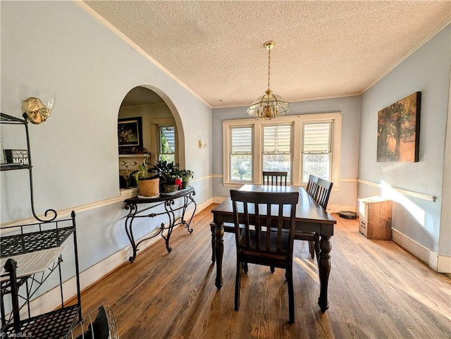 dining space with wood-type flooring, a textured ceiling, crown molding, and a notable chandelier