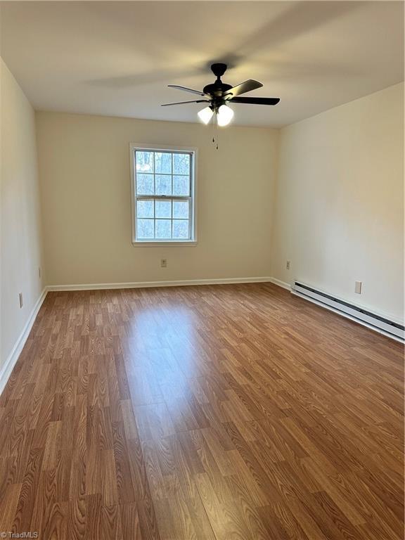 spare room featuring baseboard heating, ceiling fan, and wood-type flooring