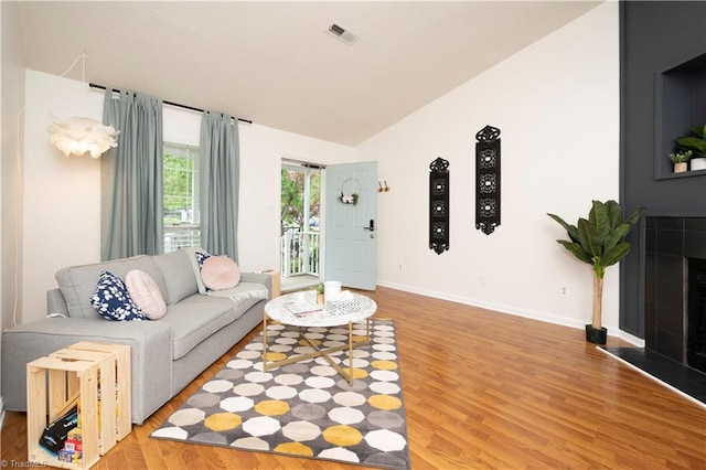 living room with a tiled fireplace, lofted ceiling, and hardwood / wood-style flooring