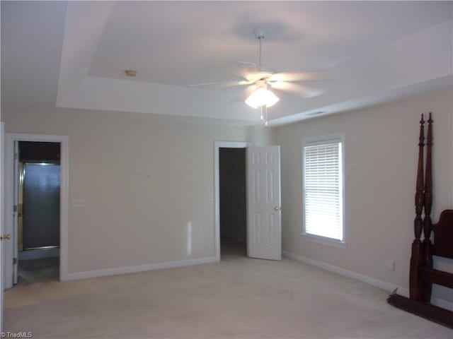 unfurnished bedroom with a walk in closet, light colored carpet, a raised ceiling, ceiling fan, and a closet