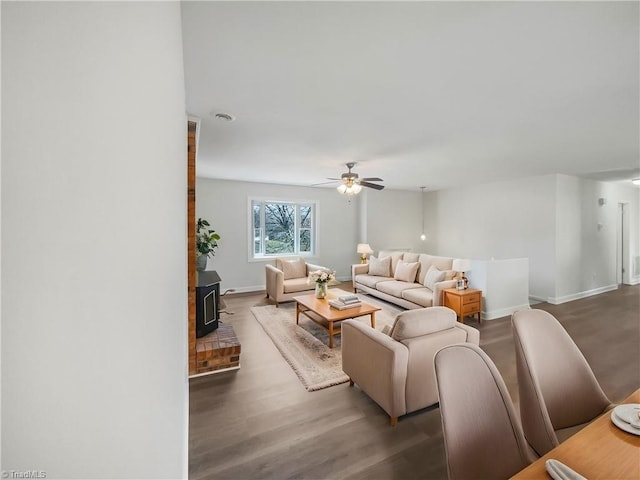 living area with a wood stove, a ceiling fan, baseboards, and wood finished floors