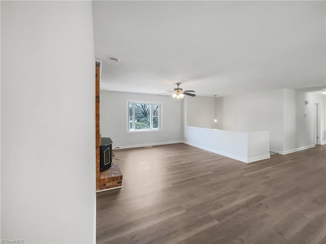 unfurnished living room featuring ceiling fan, wood finished floors, a wood stove, and baseboards