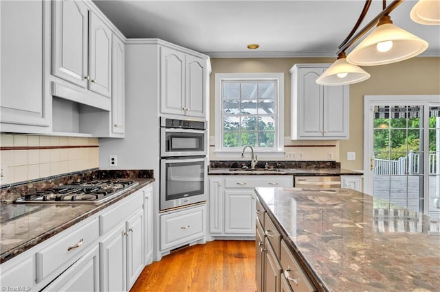 kitchen with appliances with stainless steel finishes, dark stone countertops, a sink, light wood finished floors, and white cabinets