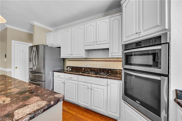 kitchen featuring stainless steel appliances, ornamental molding, decorative backsplash, white cabinetry, and dark stone countertops