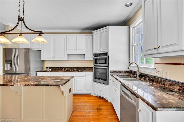 kitchen with appliances with stainless steel finishes, a sink, decorative light fixtures, a kitchen island, and tasteful backsplash