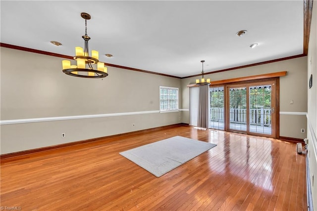 empty room featuring a chandelier, wood-type flooring, baseboards, and crown molding