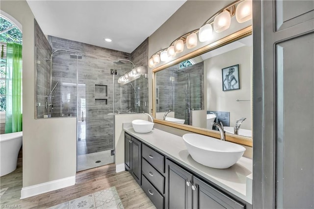 full bath featuring a stall shower, double vanity, a soaking tub, wood finished floors, and recessed lighting