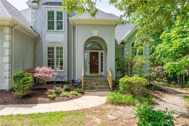 property entrance featuring stucco siding and a shingled roof