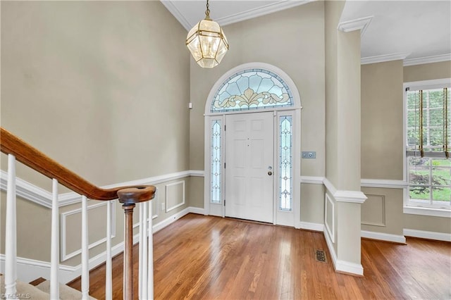 foyer entrance featuring wood finished floors, crown molding, a chandelier, and stairs