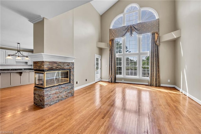 unfurnished living room featuring light wood-style flooring, healthy amount of natural light, high vaulted ceiling, baseboards, and a fireplace