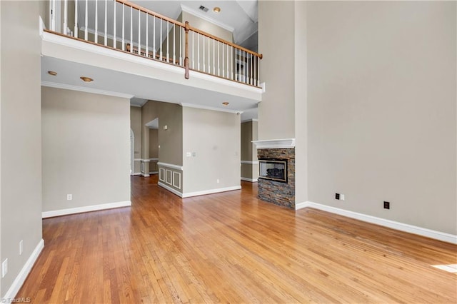 unfurnished living room with wood-type flooring, a high ceiling, ornamental molding, a stone fireplace, and baseboards