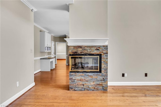 unfurnished living room with ornamental molding, baseboards, light wood finished floors, and a fireplace