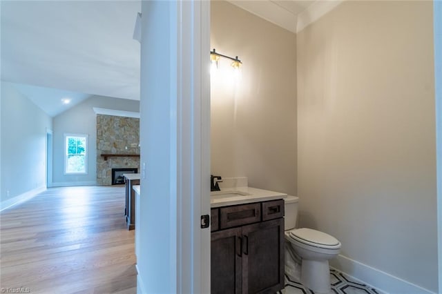 bathroom featuring vaulted ceiling, a fireplace, hardwood / wood-style floors, vanity, and toilet