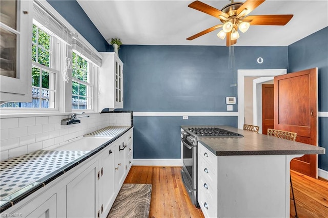 kitchen with stainless steel gas range, a sink, light wood finished floors, glass insert cabinets, and baseboards