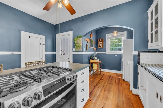kitchen featuring gas stove, a ceiling fan, light wood-style floors, freestanding refrigerator, and glass insert cabinets