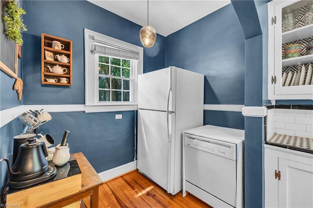 kitchen with white appliances, wood finished floors, backsplash, hanging light fixtures, and baseboards
