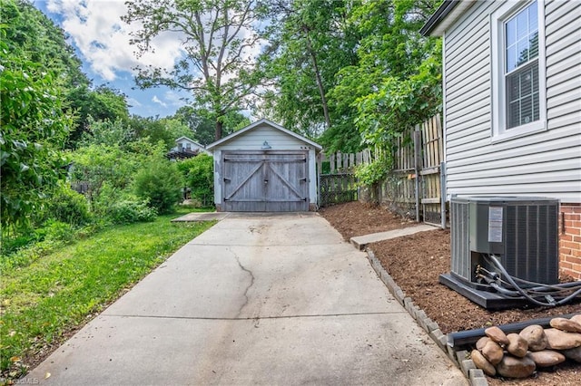 view of yard with central AC, a storage unit, an outbuilding, fence, and concrete driveway