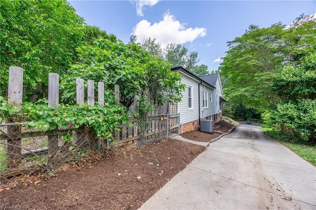 view of side of property with fence, concrete driveway, and central AC