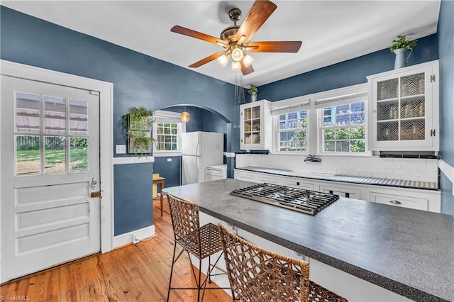 kitchen featuring freestanding refrigerator, stainless steel gas stovetop, white cabinetry, and light wood-style floors