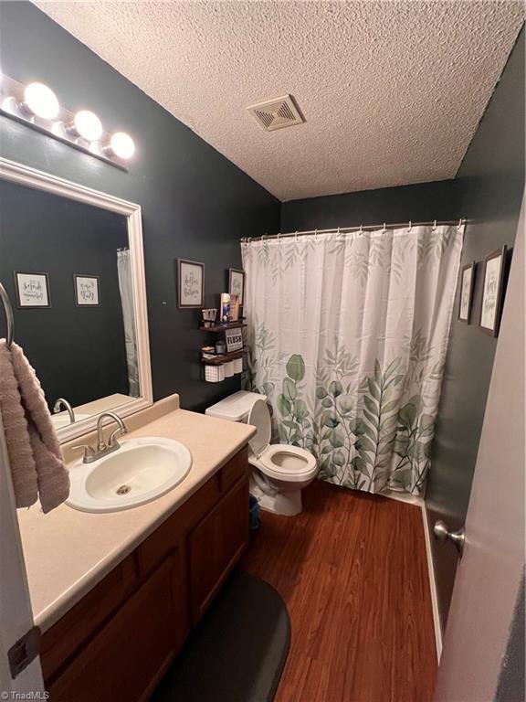 bathroom featuring vanity, wood-type flooring, a textured ceiling, vaulted ceiling, and toilet