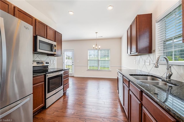 kitchen featuring dark stone counters, dark wood finished floors, appliances with stainless steel finishes, decorative light fixtures, and a sink