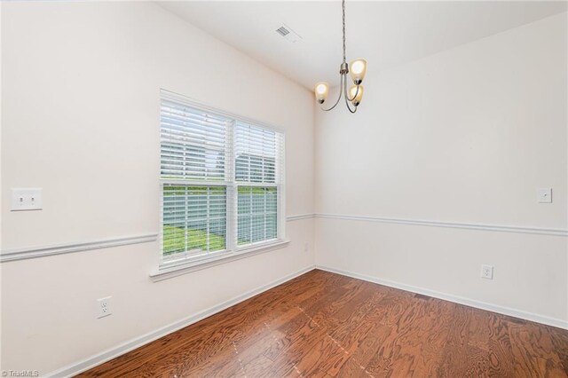 empty room featuring baseboards, wood finished floors, visible vents, and a notable chandelier