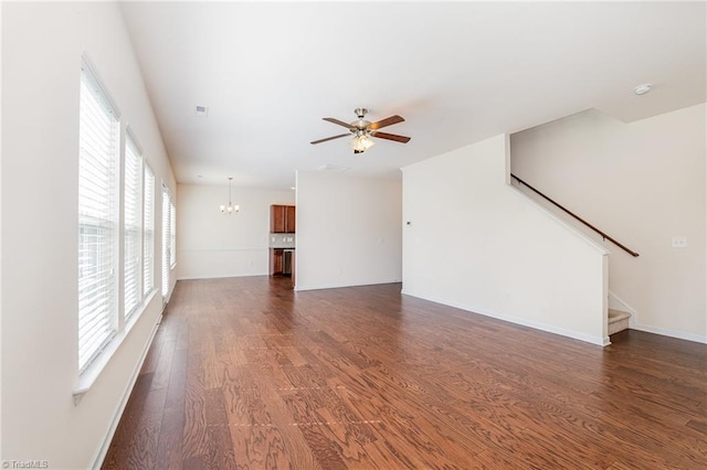 unfurnished living room with visible vents, baseboards, dark wood-style floors, stairs, and ceiling fan with notable chandelier