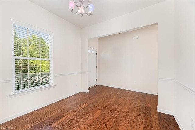 unfurnished room with dark wood-style floors, a notable chandelier, and baseboards