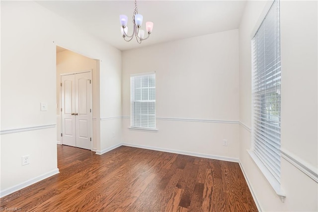 empty room with a notable chandelier, baseboards, and dark wood-style flooring