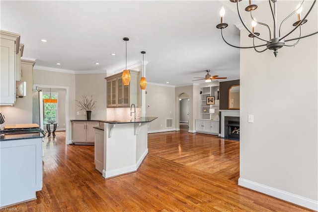 kitchen with a peninsula, wood finished floors, dark countertops, a breakfast bar area, and arched walkways