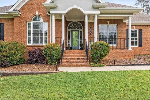 property entrance featuring brick siding, roof with shingles, and a lawn