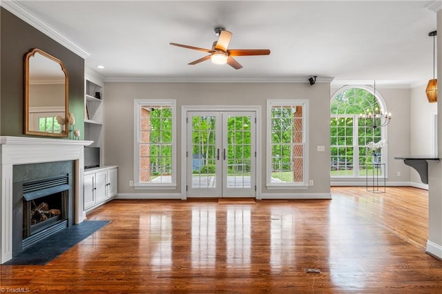 unfurnished living room featuring crown molding, ceiling fan with notable chandelier, baseboards, a fireplace with flush hearth, and wood finished floors