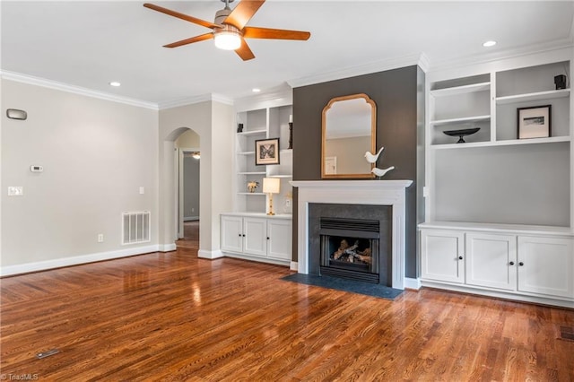 unfurnished living room with a ceiling fan, visible vents, arched walkways, built in shelves, and ornamental molding