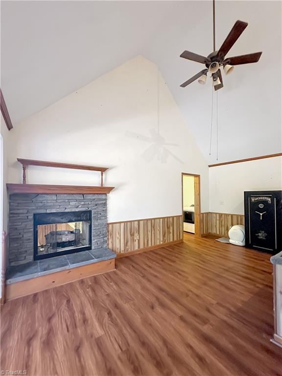 unfurnished living room featuring ceiling fan, hardwood / wood-style flooring, high vaulted ceiling, a fireplace, and wooden walls