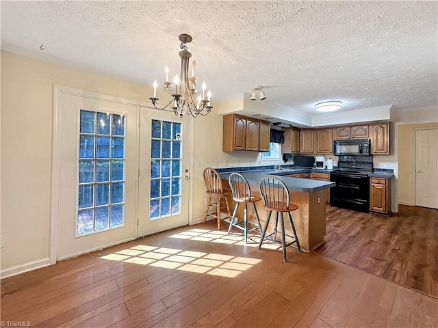 kitchen with a kitchen bar, black appliances, kitchen peninsula, and dark hardwood / wood-style floors