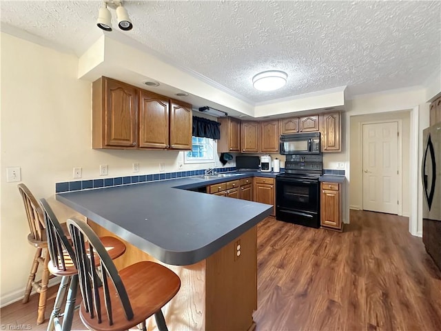 kitchen with dark wood-type flooring, kitchen peninsula, sink, black appliances, and a textured ceiling