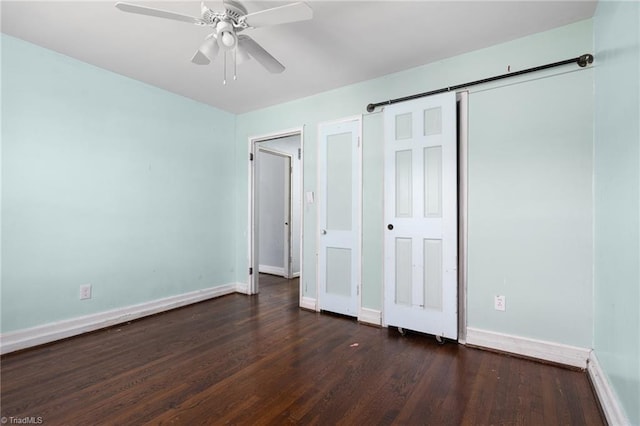 unfurnished bedroom featuring a barn door, dark hardwood / wood-style floors, and ceiling fan