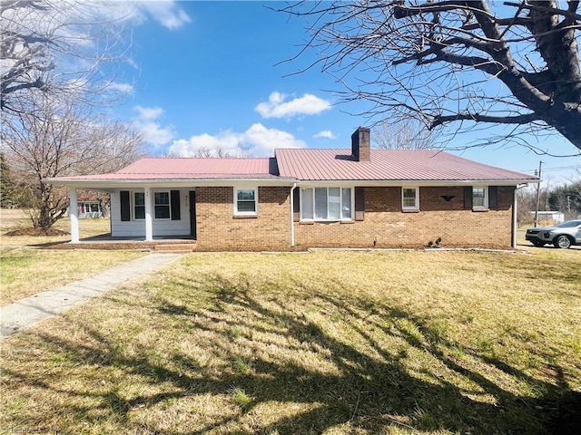 view of front facade featuring brick siding, a chimney, covered porch, metal roof, and a front lawn