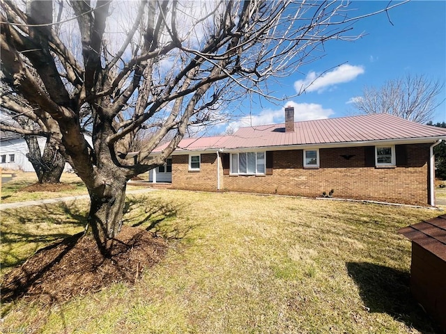 view of side of property featuring a yard, metal roof, brick siding, and a chimney