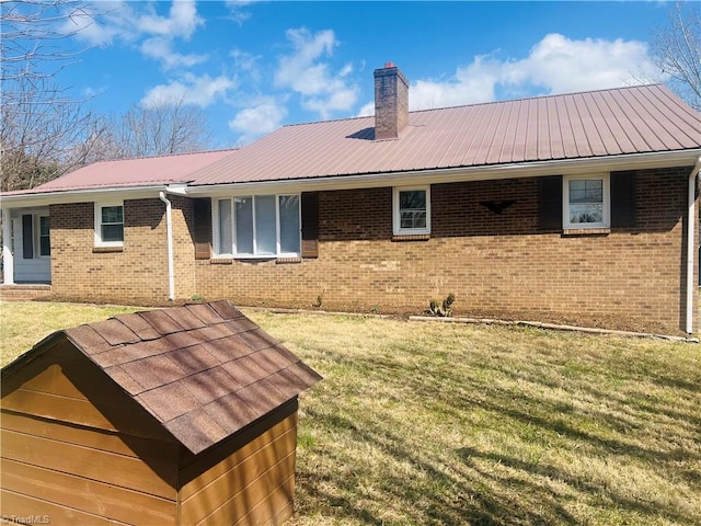 rear view of property with a chimney, metal roof, a lawn, and brick siding