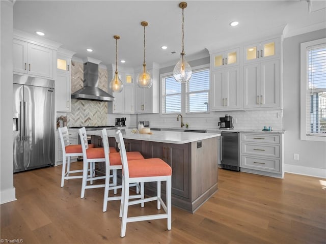 kitchen featuring stainless steel built in refrigerator, white cabinetry, a kitchen island, and wall chimney exhaust hood