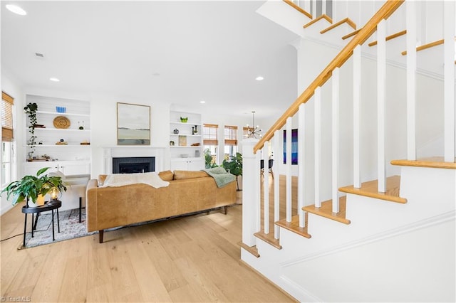 living room featuring built in shelves, a notable chandelier, light hardwood / wood-style flooring, and a wealth of natural light