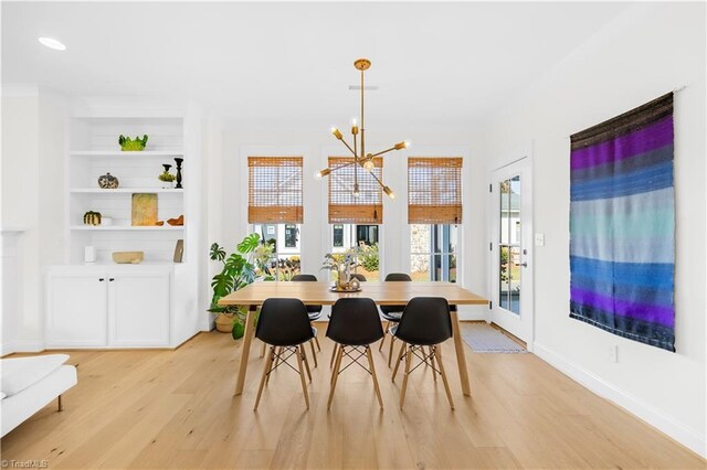 dining room with built in shelves, a chandelier, and light hardwood / wood-style flooring