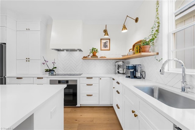 kitchen with appliances with stainless steel finishes, white cabinetry, sink, custom exhaust hood, and light hardwood / wood-style flooring