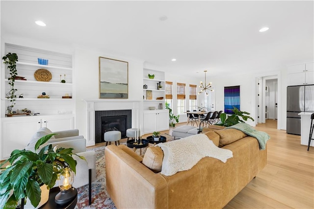 living room featuring an inviting chandelier, built in features, and light wood-type flooring