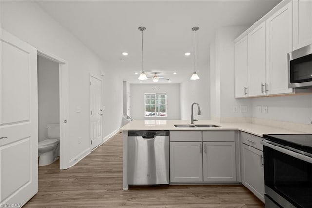 kitchen with pendant lighting, sink, light hardwood / wood-style flooring, stainless steel appliances, and kitchen peninsula