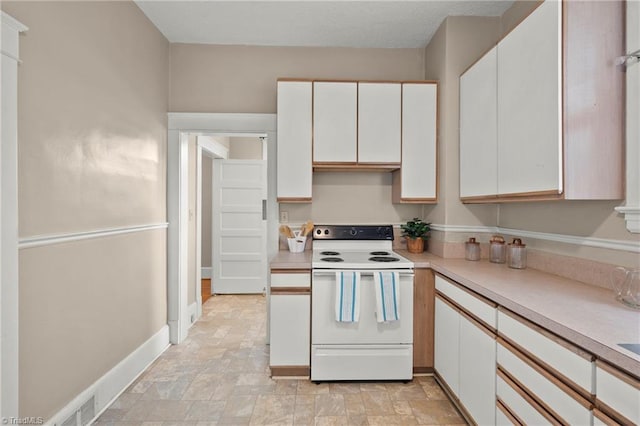 kitchen featuring white electric range oven, white cabinetry, light countertops, and stone finish floors