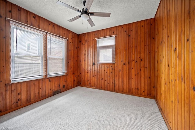 unfurnished room featuring healthy amount of natural light, ceiling fan, wood walls, a textured ceiling, and carpet floors